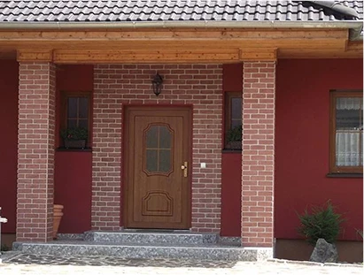 Klasické vstupní dveře v dekoru dřeva zasazené do cihlového portálu rodinného domu